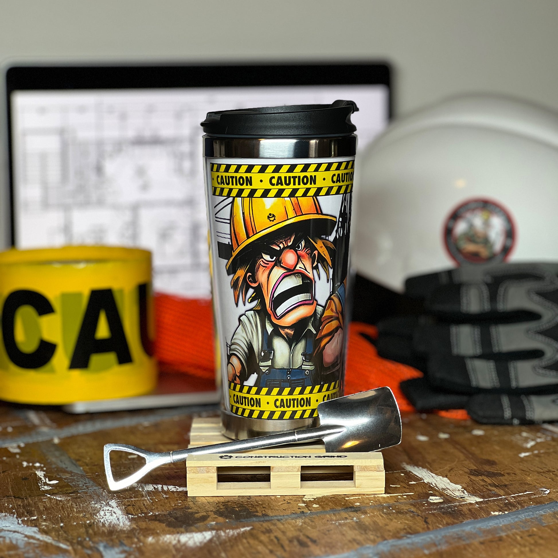 Construction Grind's "Meet the Crew" Second Shift 12 oz. coffee tumbler sitting on a 4" wooden pallet coaster with a stainless-steel shovel spoon. Showing our Site Superintendent, "Jack", one of three crew members shown on the tumbler.