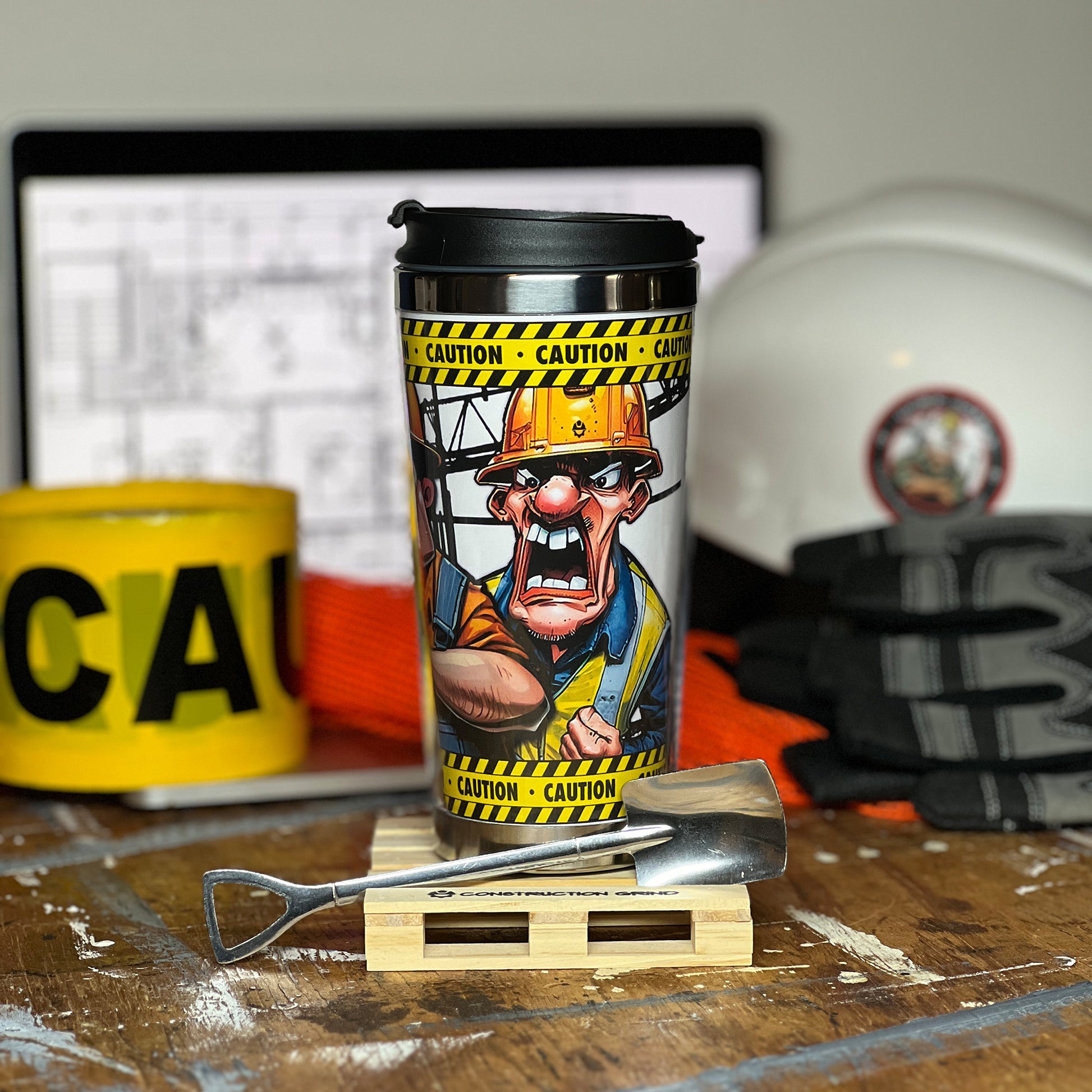 Construction Grind's "Meet the Crew" Second Shift 12 oz. coffee tumbler sitting on a 4" wooden pallet coaster with a stainless-steel shovel spoon. Showing our Safety Manager, "Danny", one of three crew members shown on the tumbler.