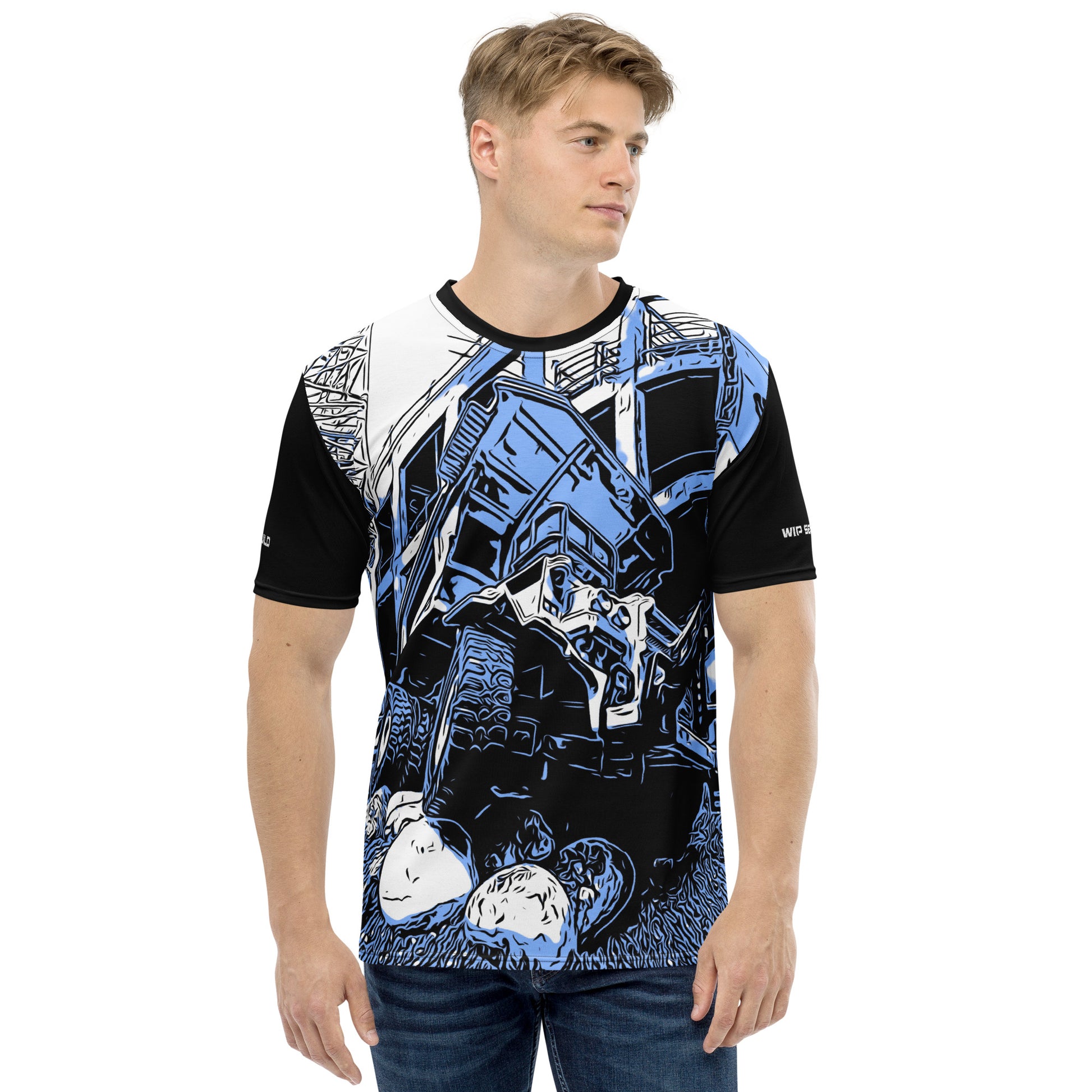 A man wearing our Construction Grind Big Dump all-over print short-sleeved t-shirt in our blue jeans style, shown from the front. The main graphic features a large dump truck actively crawling over rough terrain at a construction site in front of a building under construction, highlighting dynamic construction imagery. The design is printed in vibrant colors on a premium, all-over print tee.