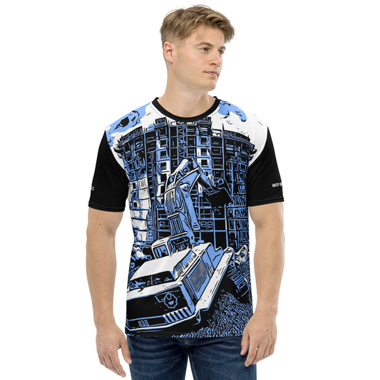 A man wearing our Construction Grind Dig Alert all-over print short-sleeved t-shirt in our blue jeans style, shown from the front. The main graphic features a large excavator actively digging rough terrain at a construction site in front of a building under construction, highlighting dynamic construction imagery. The design is printed in vibrant colors on a premium, all-over print tee.