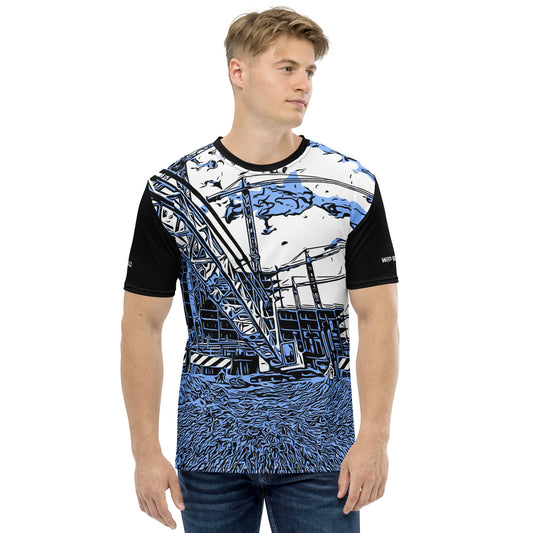 A man wearing our Construction Grind Heavy Lift all-over print short-sleeved t-shirt in our blue jeans style, shown from the front. The main graphic features a large crane at a construction site in front of a building under construction, highlighting dynamic construction imagery. The design is printed in vibrant colors on a premium, all-over print tee.