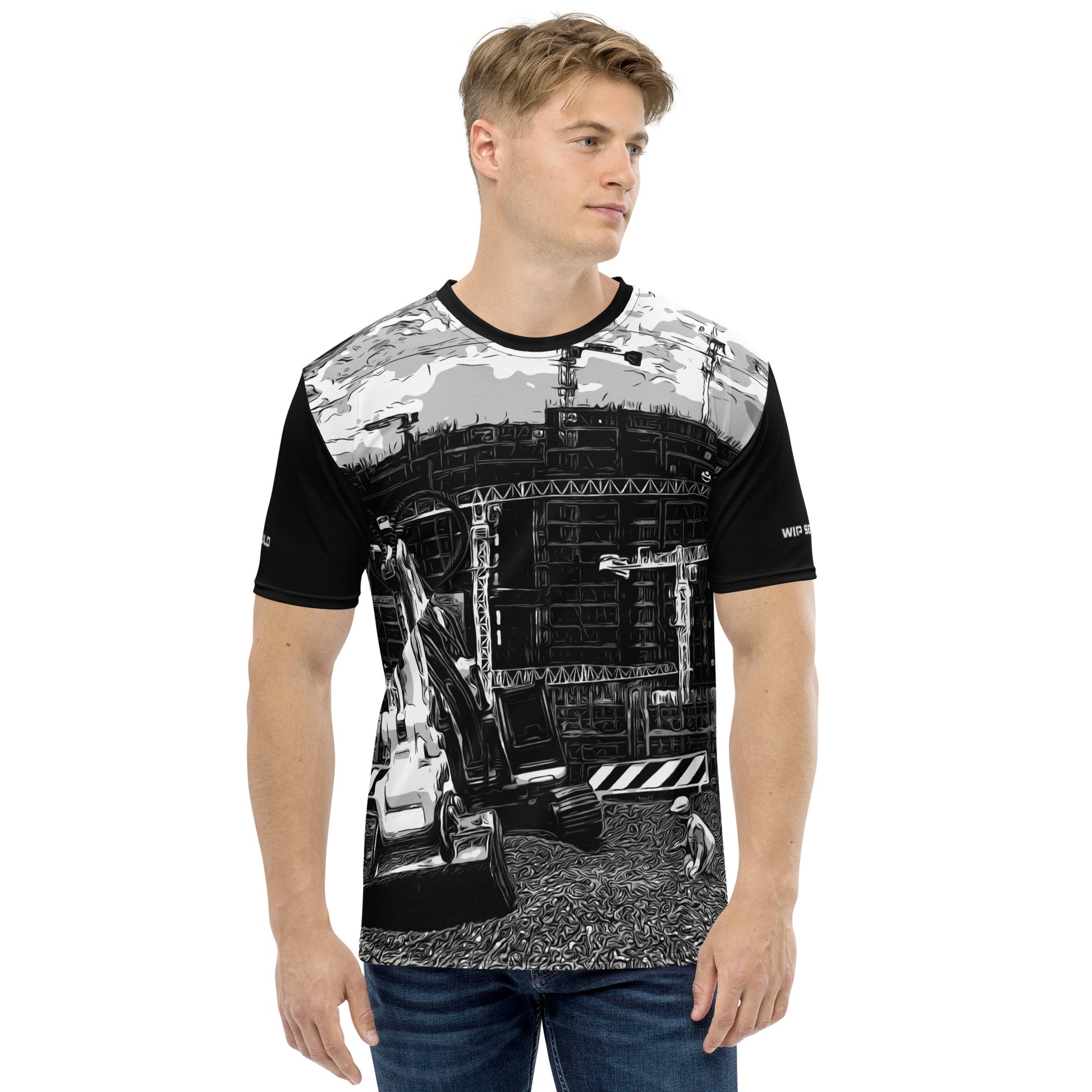 A man wearing our Construction Grind Trenching all-over print short-sleeved t-shirt in our black and white style, shown from the front. The main graphic features a backhoe digging a trench in front of large tower cranes at a construction site in front of a building under construction, highlighting dynamic construction imagery. The design is printed in vibrant colors on a premium, all-over print tee.