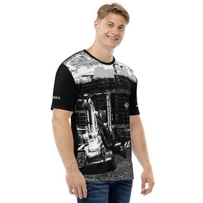 A man wearing our Construction Grind Trenching all-over print short-sleeved t-shirt in black and white style, shown from the right-hand view. The image reveals the detailed main graphic of a backhoe in action on a construction site, and the right sleeve displays a white 'I Build' graphic. The design emphasizes bold construction imagery on a premium tee.