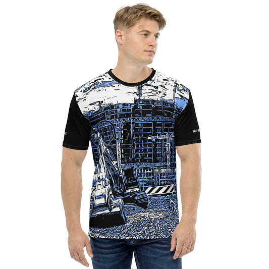 A man wearing our Construction Grind Trenching all-over print short-sleeved t-shirt in our blue jeans style, shown from the front. The main graphic features a backhoe digging a trench in front of large tower cranes at a construction site in front of a building under construction, highlighting dynamic construction imagery. The design is printed in vibrant colors on a premium, all-over print tee.